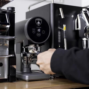 Eureka Disko electric coffee tamper in black with a portafilter being set into the holder by hand