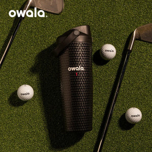 Owala Out of Bounds golf bottle on grass with golf clubs and golf balls