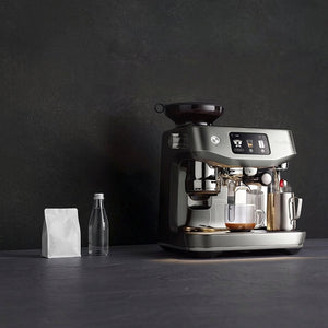 Breville espresso machine with grinder, front angled view on a counter beside a water bottle and coffee bag