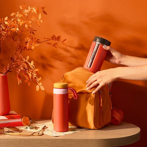 Orange insulated travel mug held next to bag and accessories