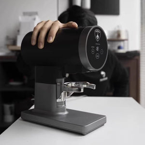 Hand resting on top of the black Eureka Disko electric tamper, side angle
